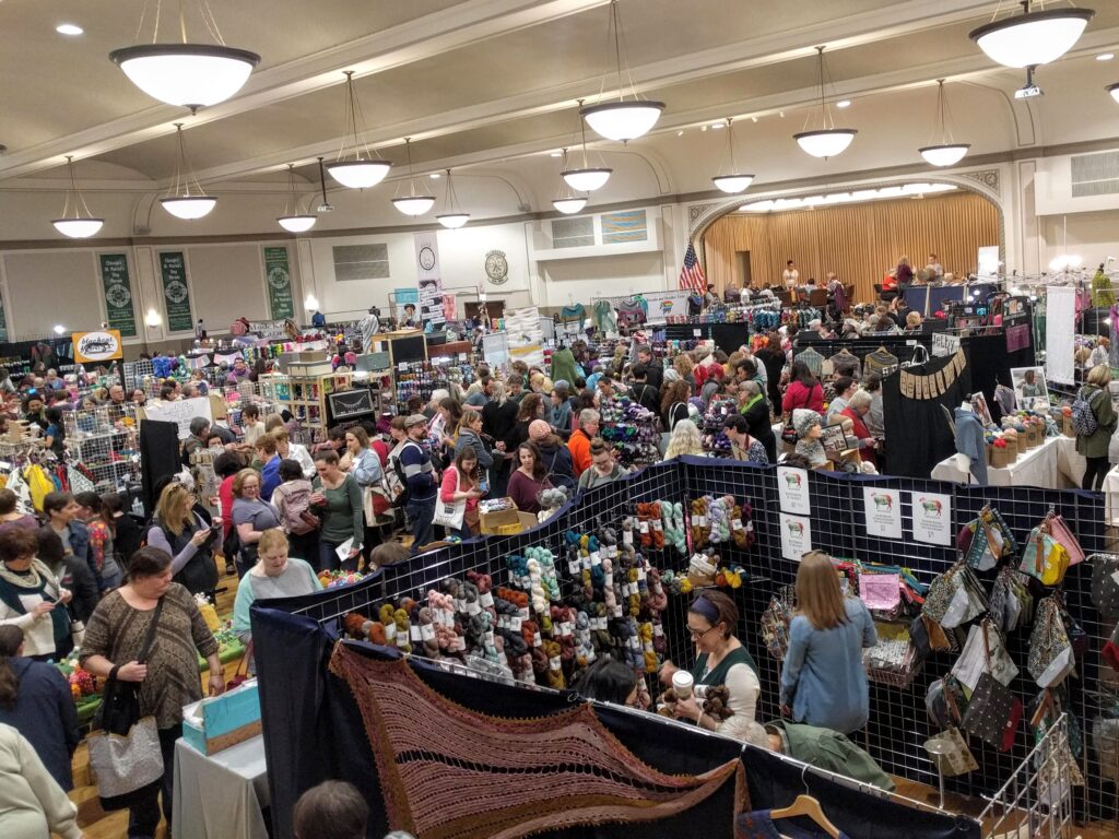 The ballroom at the Plumbers Union Hall full of YarnCon vendor booths and shoppers. The room is full of happy people and so much yarn.